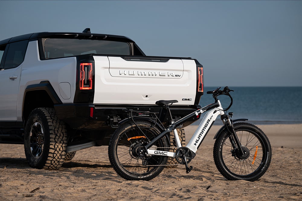 The AWD Electric Bike is parked on the sand, behind the Hummer EV.